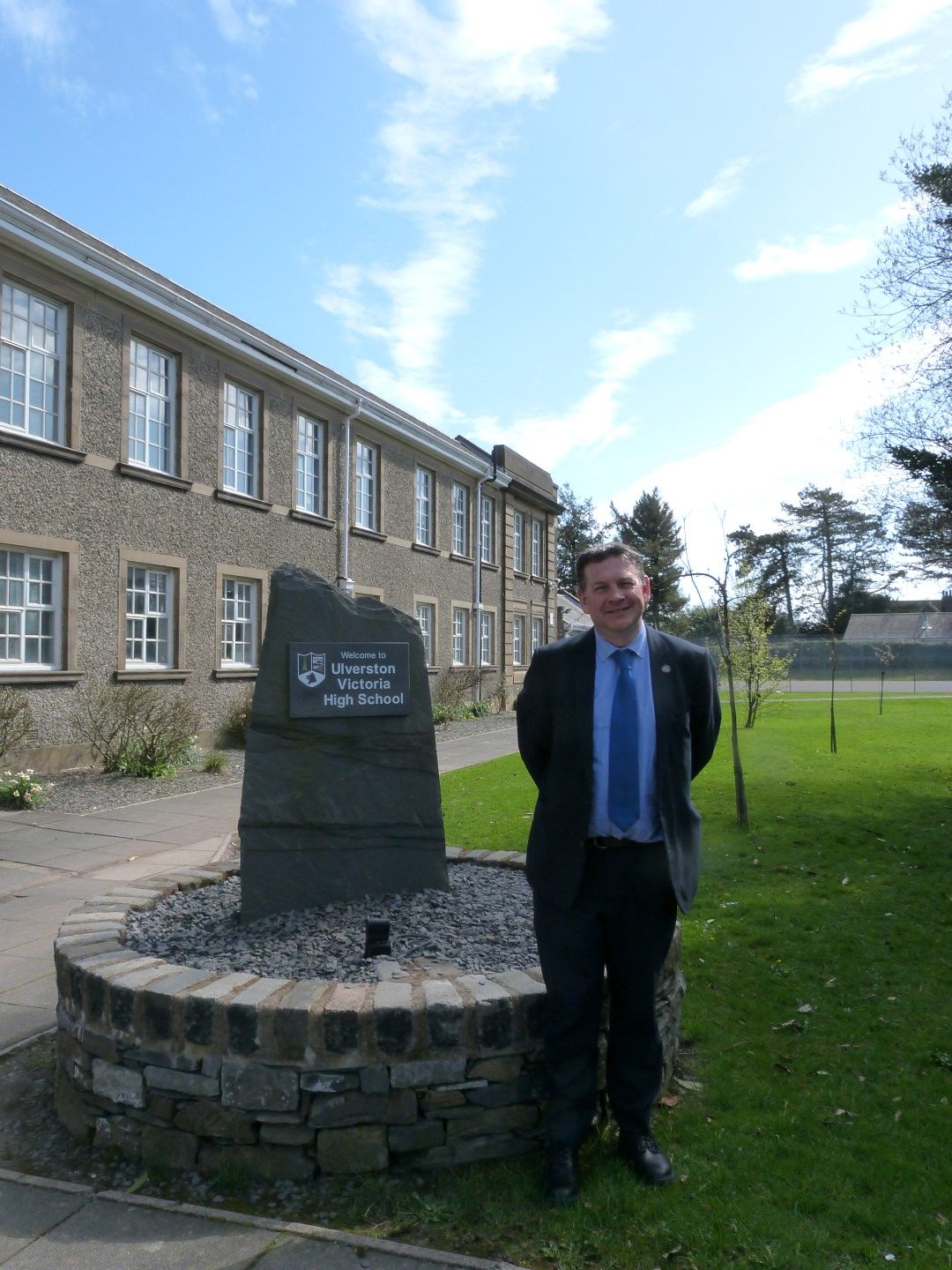 Picture of Headteacher Mr Hardwick next to a slate column with school name and logo on it.